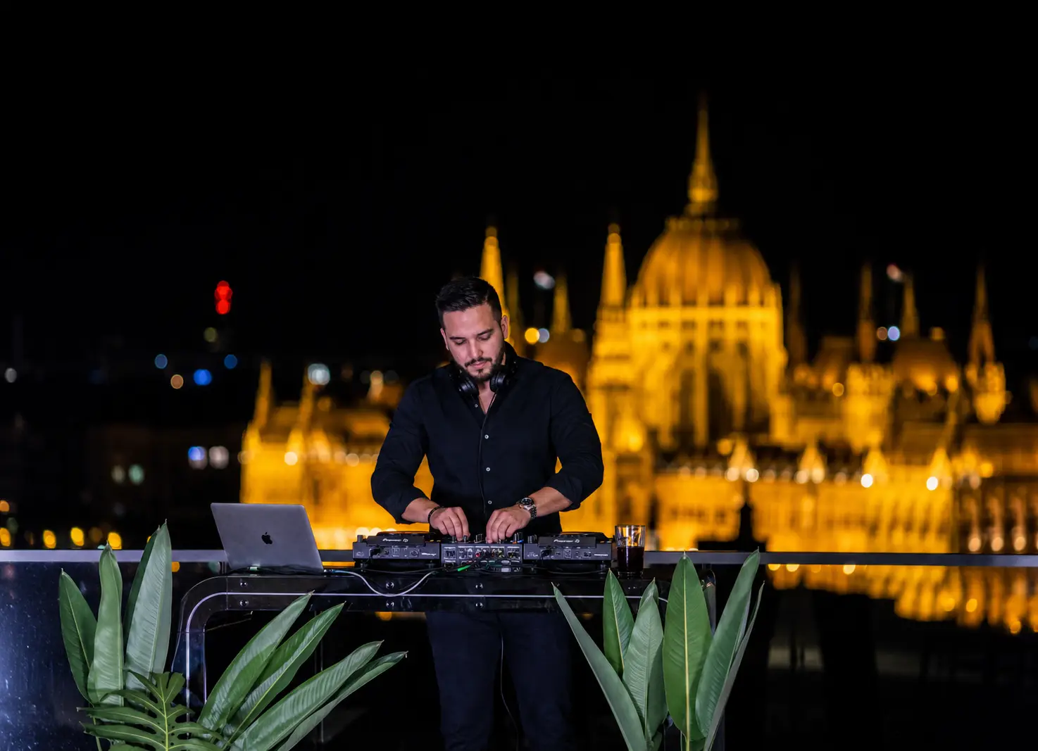 DJ pult mögött játszó zenész éjszaka, háttérben a kivilágított Országház